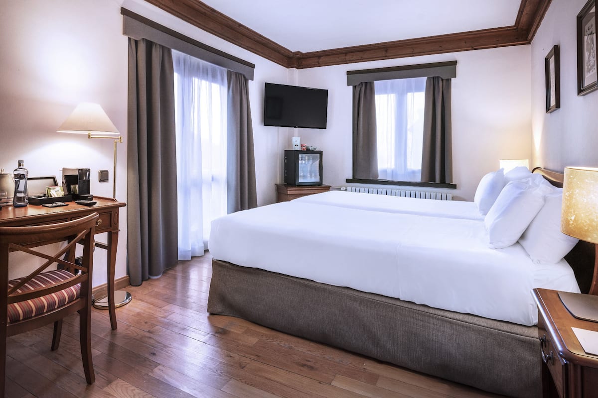 Una habitación de hotel con una cama grande, un escritorio con una silla, un televisor y una ventana con cortinas.