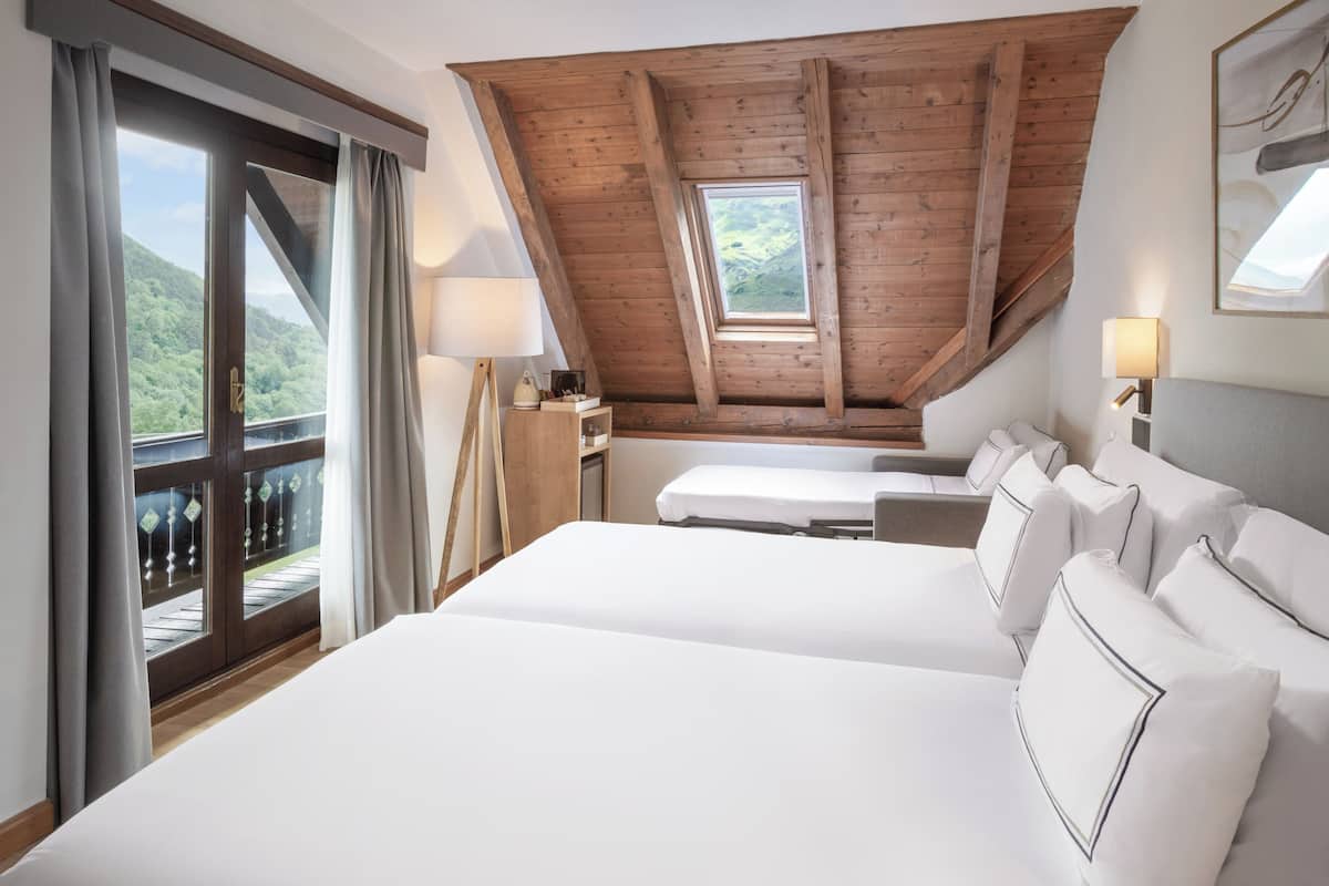 Un dormitorio con una cama grande, un escritorio y vistas a la montaña a través de una ventana.
