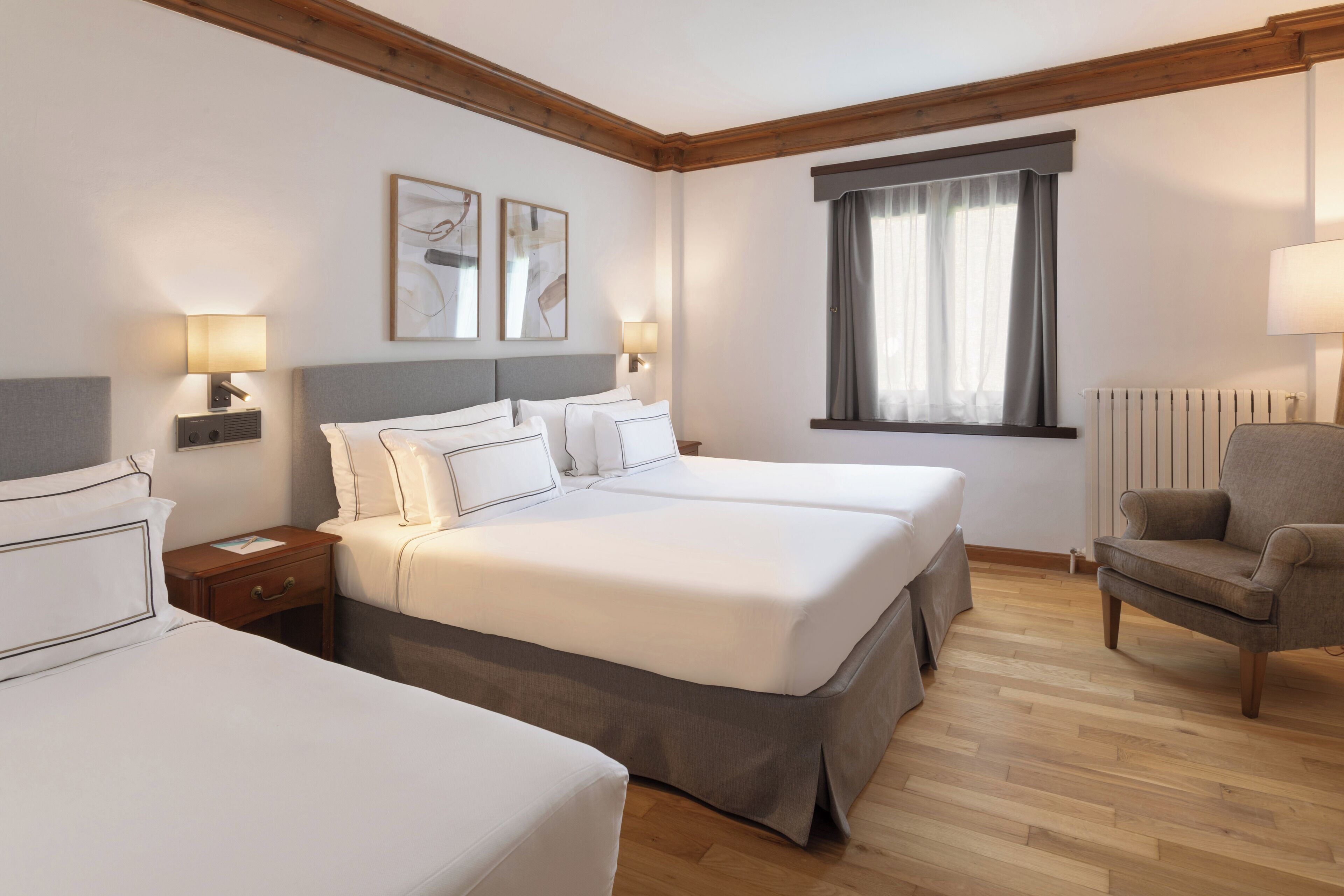 A hotel room with two beds, a chair, and a window with curtains.