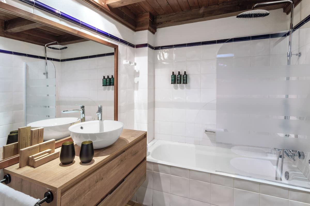 Un baño moderno con tocador de madera, dos lavamanos, una bañera y una ducha.