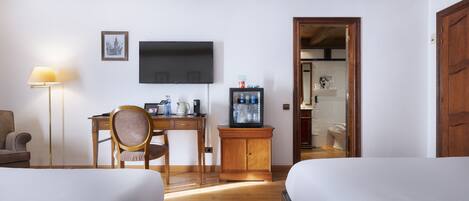 Une chambre d’hôtel avec deux lits, un bureau avec une chaise, une télévision, une lampe et une salle de bain visible à travers une porte ouverte.