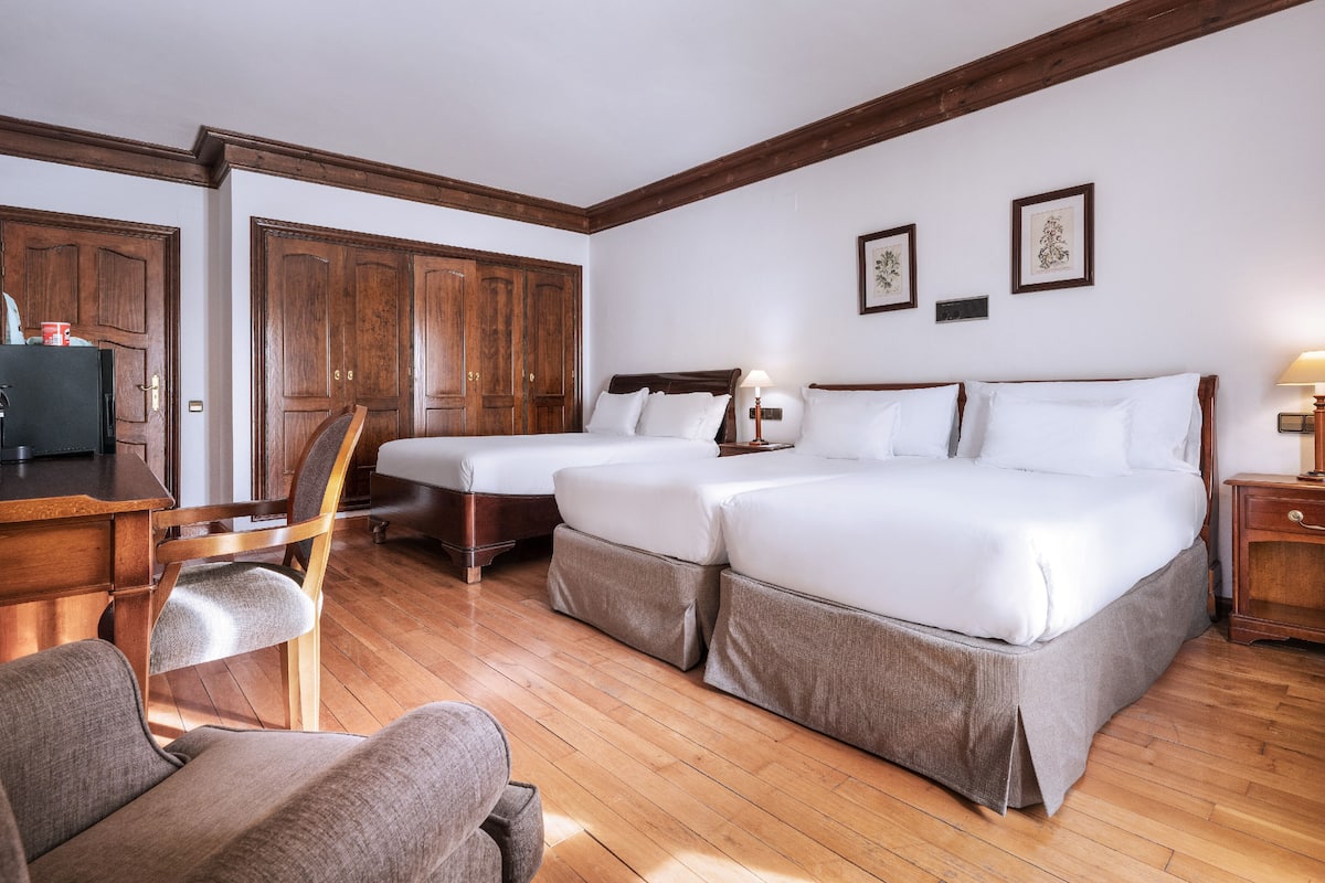 Habitación de hotel con dos camas individuales, un escritorio con silla y suelo de madera.