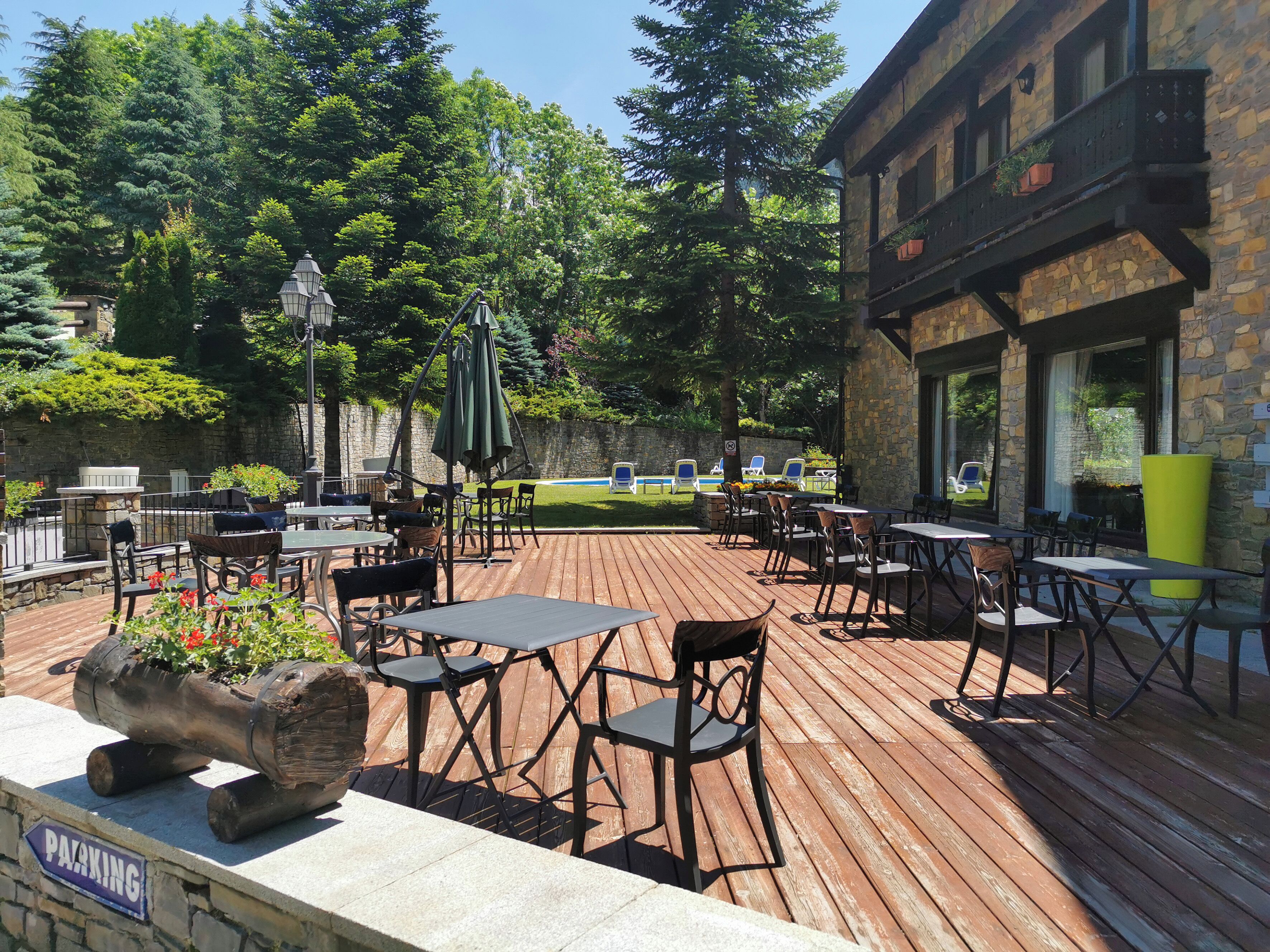 An outdoor patio with tables and chairs, a stone building, and a pool in the background.