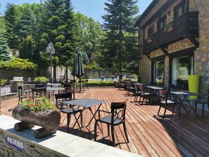 An outdoor patio with tables and chairs, a stone building, and a pool in the background.
