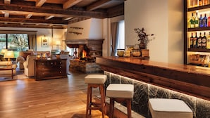 Un área de bar acogedor con vigas de madera, una chimenea de piedra y una barra repleta de botellas diversas.