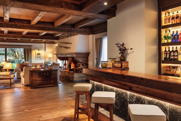 Un área de bar acogedor con vigas de madera, una chimenea de piedra y una barra repleta de botellas diversas.