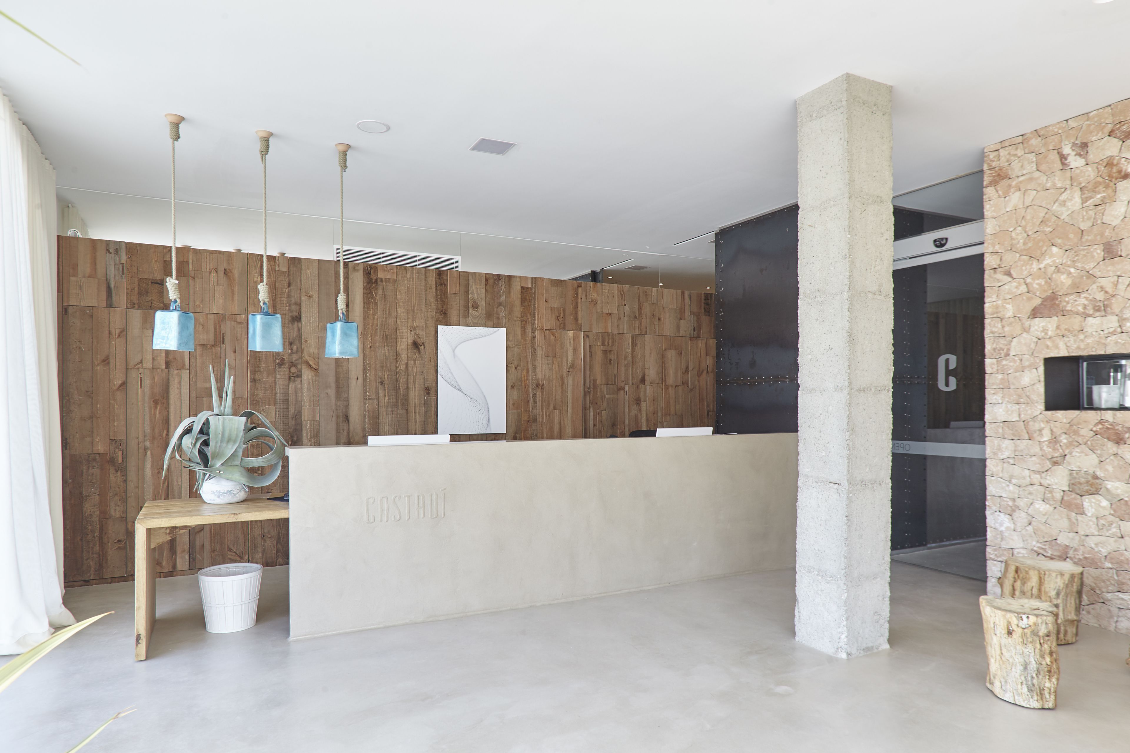 A reception area with a wooden wall, a concrete reception desk, and hanging pendant lights.