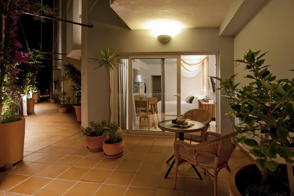 Un patio con una mesa y sillas, rodeado de plantas en macetas y una puerta corrediza de vidrio que da a una habitación.