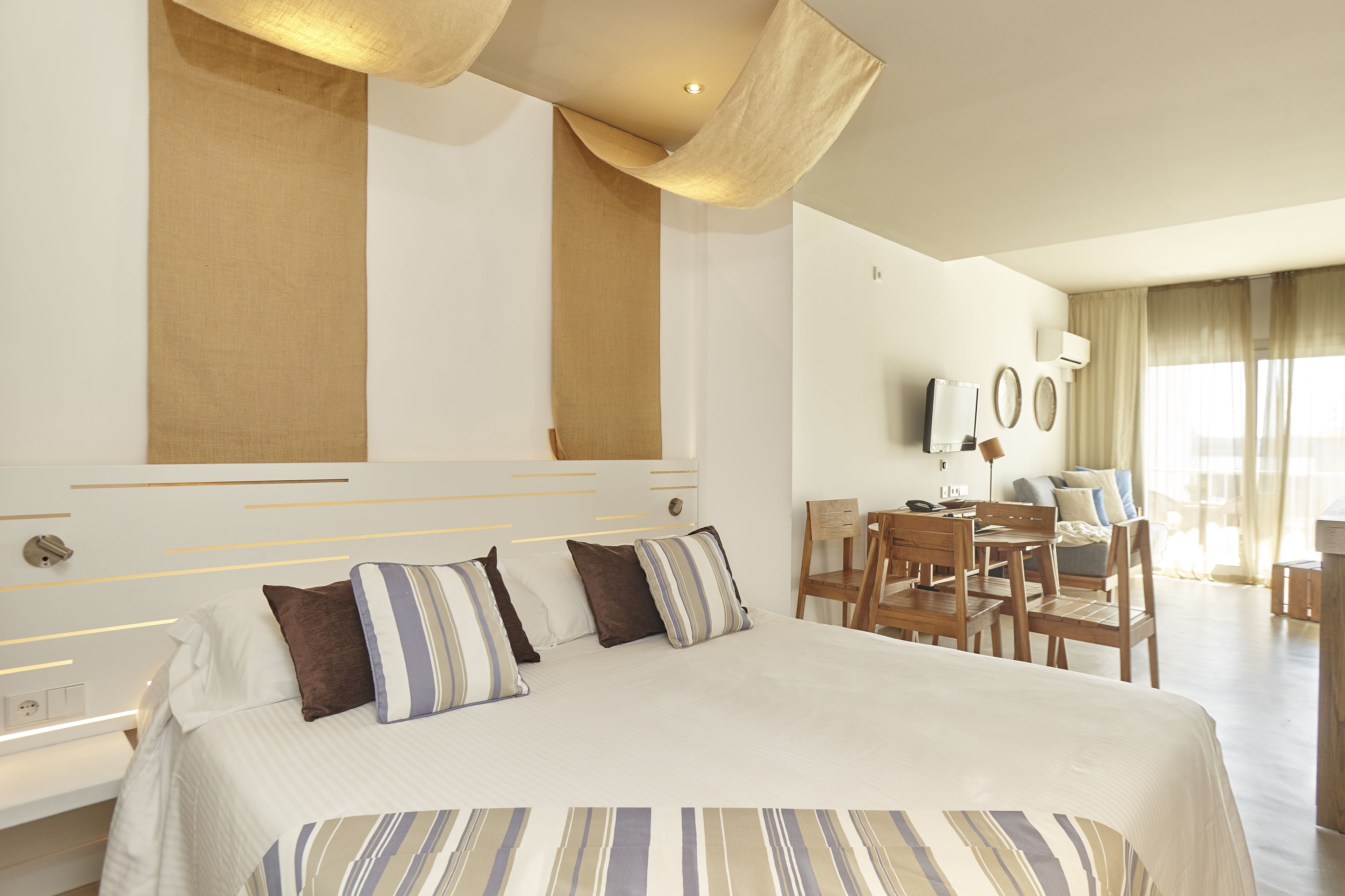 Une chambre d’hôtel avec un grand lit, un bureau et une chaise. Il y a un téléviseur accroché au mur et une fenêtre avec des rideaux.