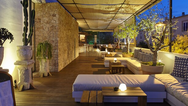 An outdoor patio with wooden flooring, a covered seating area, and potted plants. - Apartamentos Castaví (Formentera)