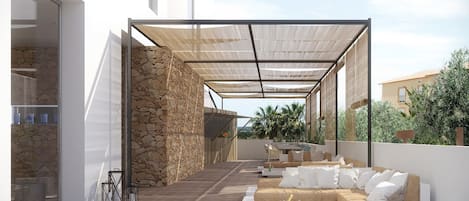 Un patio exterior con terraza de madera, sofás blancos y un muro de piedra.
