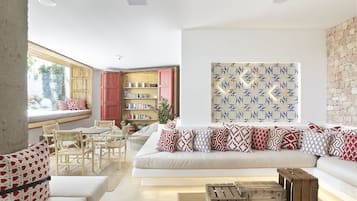 A modern living room with a white sofa, patterned cushions, wooden furniture, and a bookshelf.
