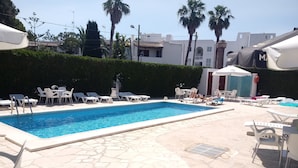 A swimming pool with lounge chairs and umbrellas, surrounded by a stone patio and palm trees. - Oasis D'or (Santanyi)