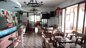 A restaurant with a bar area, multiple seating options including bar stools and tables, a chandelier, and a television on the wall. - Oasis D'or (Santanyi)