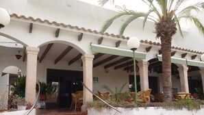 A building with a covered entrance, outdoor seating area, and a staircase leading to the entrance. - Oasis D'or (Santanyi)