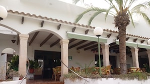 A building with a covered entrance, outdoor seating area, and a staircase leading to the entrance. - Oasis D'or (Santanyi)