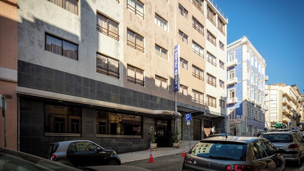 Edifício de hotel com vários andares, entrada visível e placa de estacionamento.