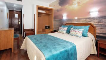 A bedroom with a bed, a desk, a wardrobe, and a mural of a sunset over the ocean.