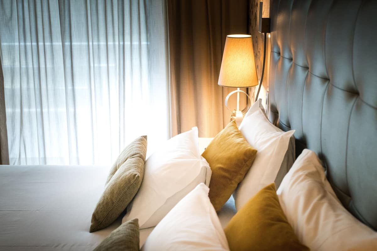 A hotel room with a bed, pillows, a lamp, and curtains.