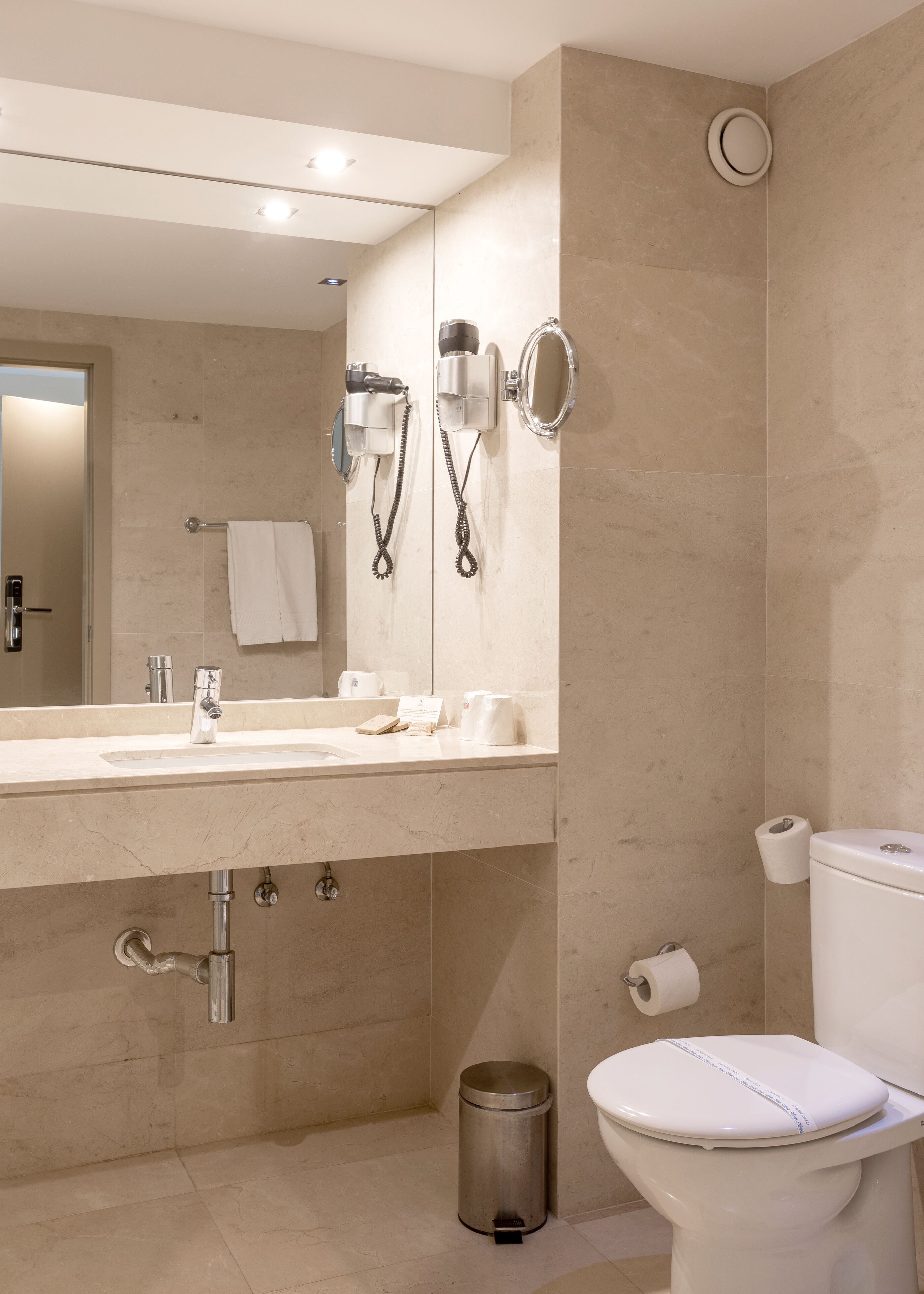 A modern bathroom with a sink, mirror, hairdryer, and toilet.