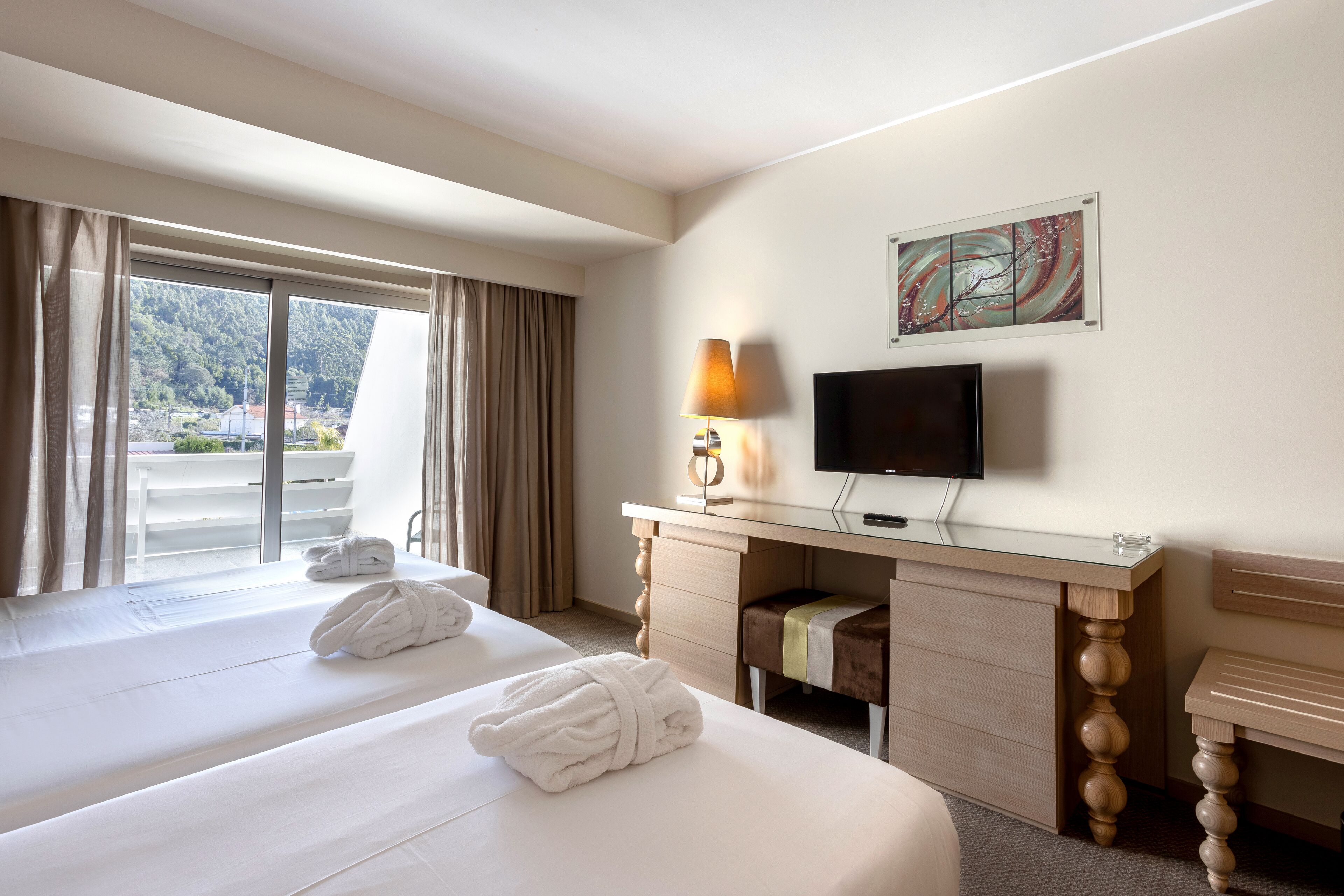 A hotel room with two beds, a desk, a TV, and a window with curtains.
