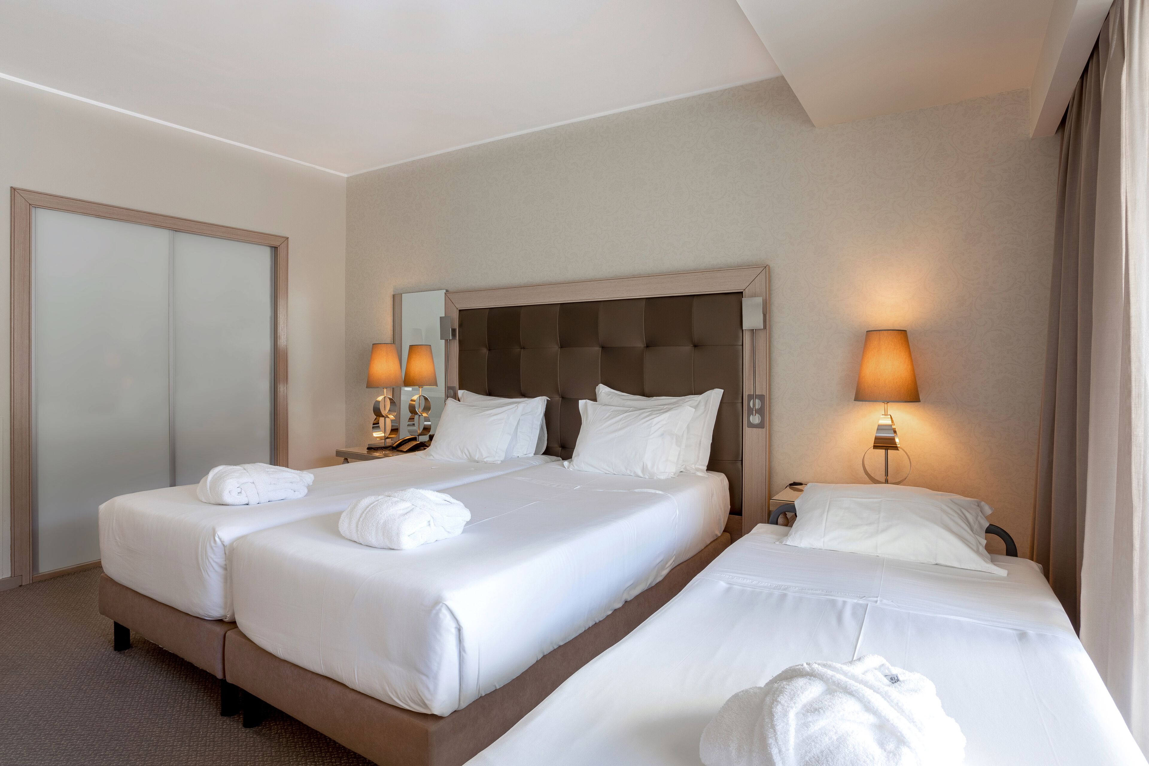 Ein Hotelzimmer mit zwei Betten, einem großen Spiegel und zwei Nachttischlampen.