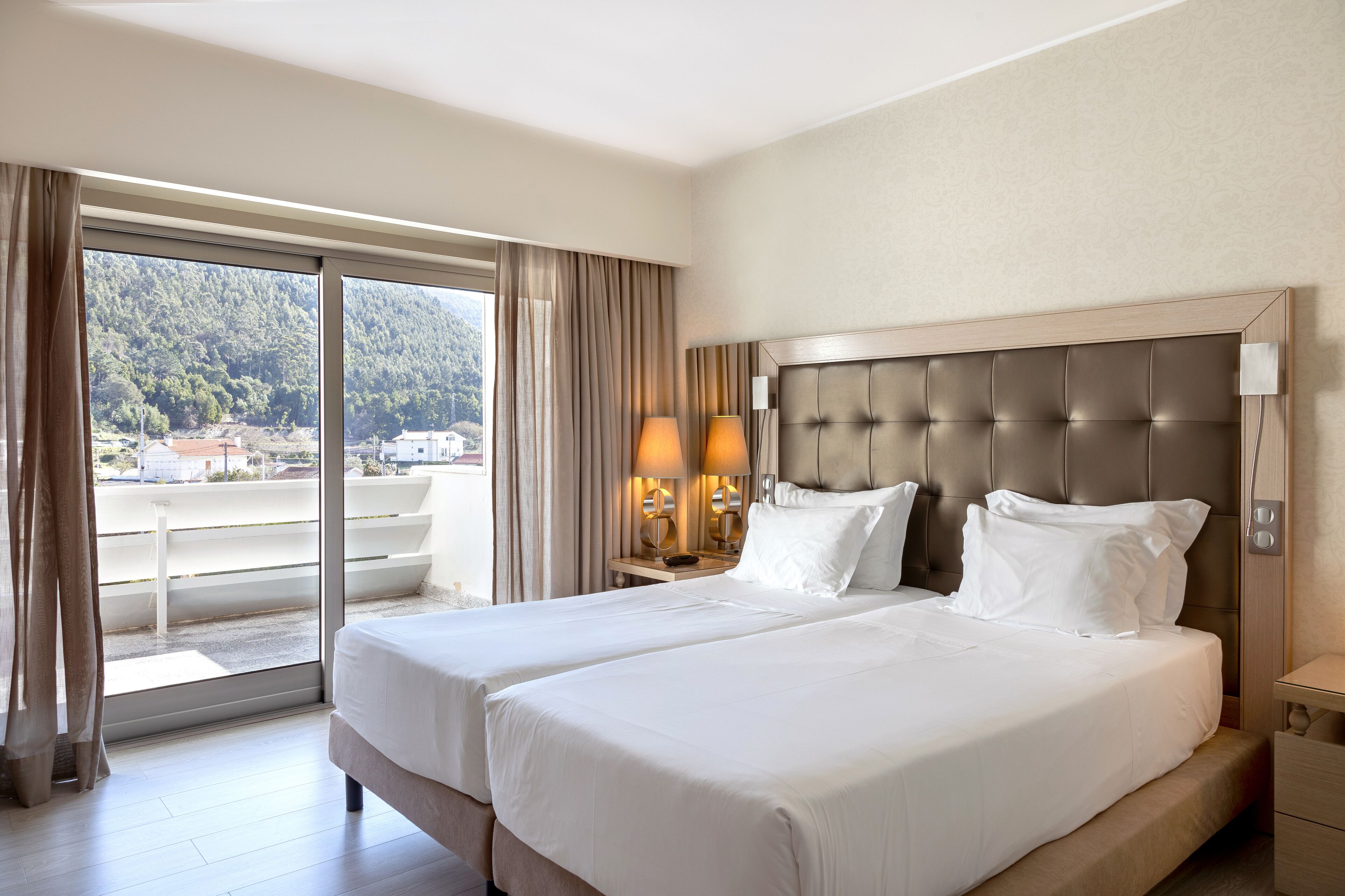 Une chambre d’hôtel avec deux lits, une grande fenêtre et une vue sur une zone boisée.