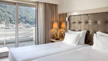 A hotel room with a large bed, two bedside lamps, a nightstand, and a view of a balcony with a mountain backdrop.