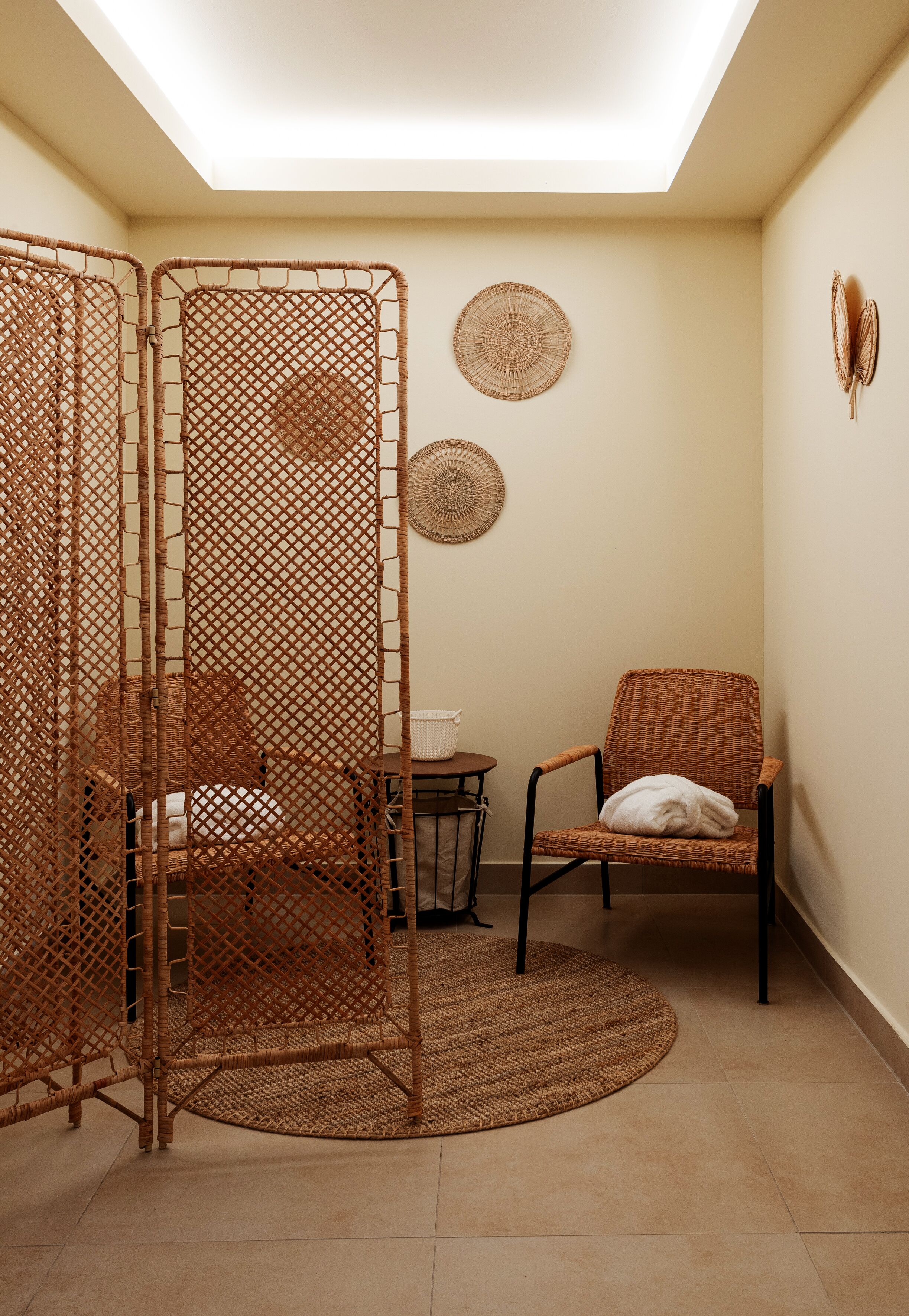 A room with a wicker partition, a wicker chair, a small round table, and woven wall decorations.