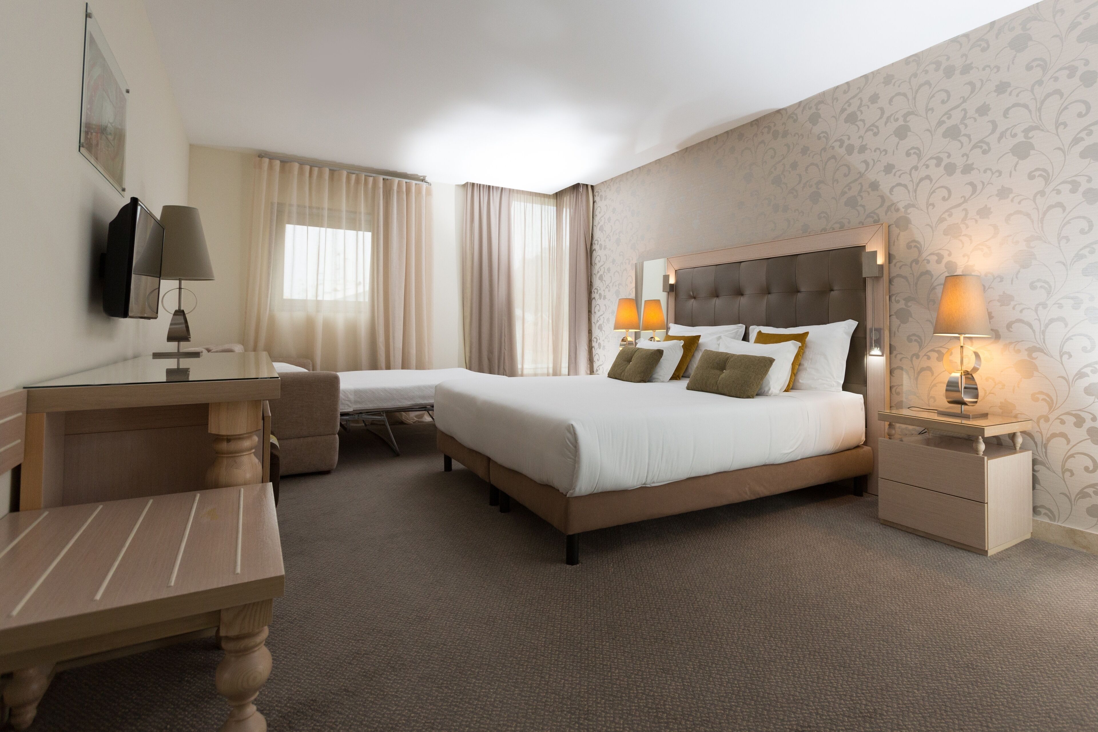 Habitación de hotel con cama, escritorio, silla, mesita de noche y televisor.