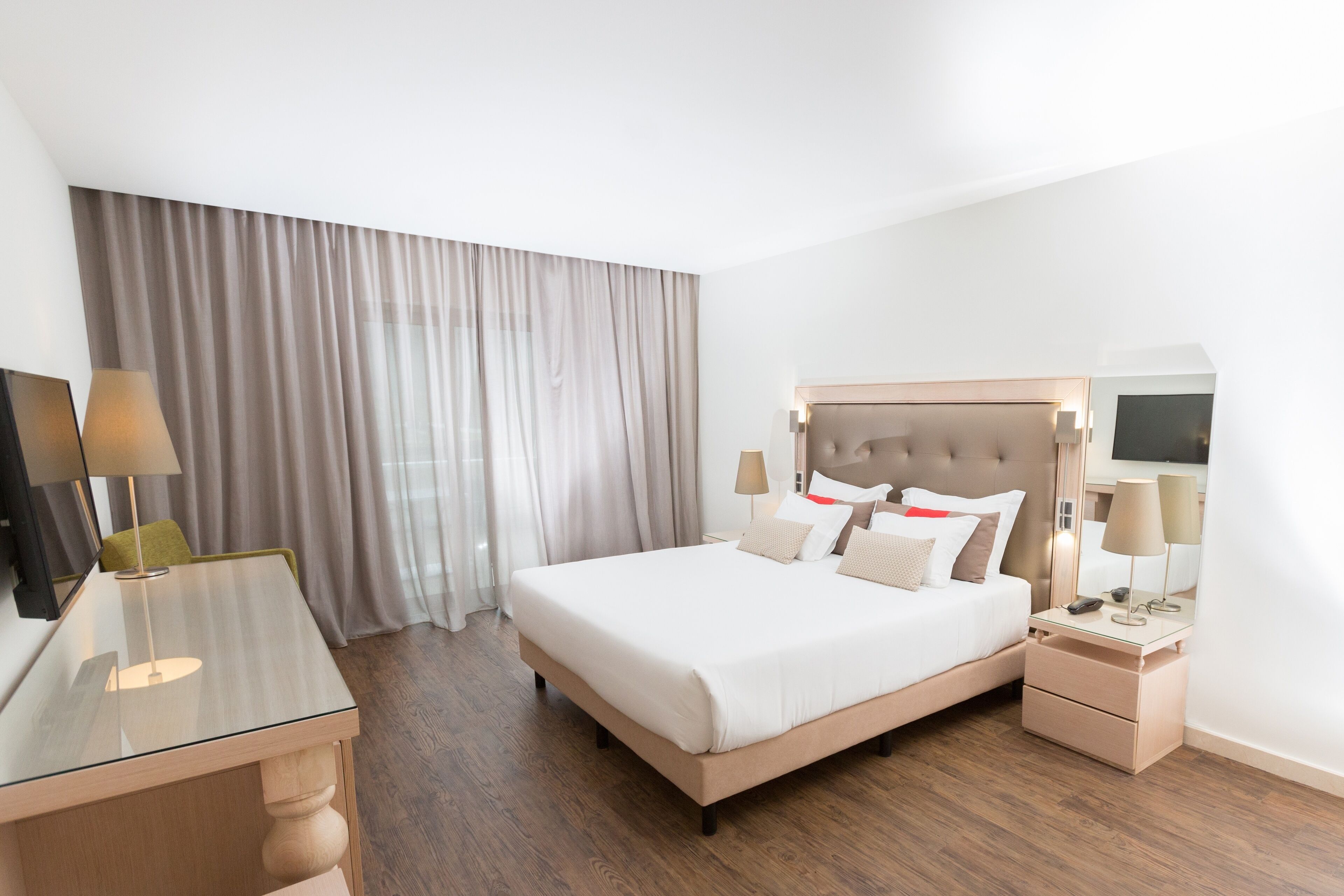 A modern hotel room with a large bed, bedside tables, a desk, and a TV.
