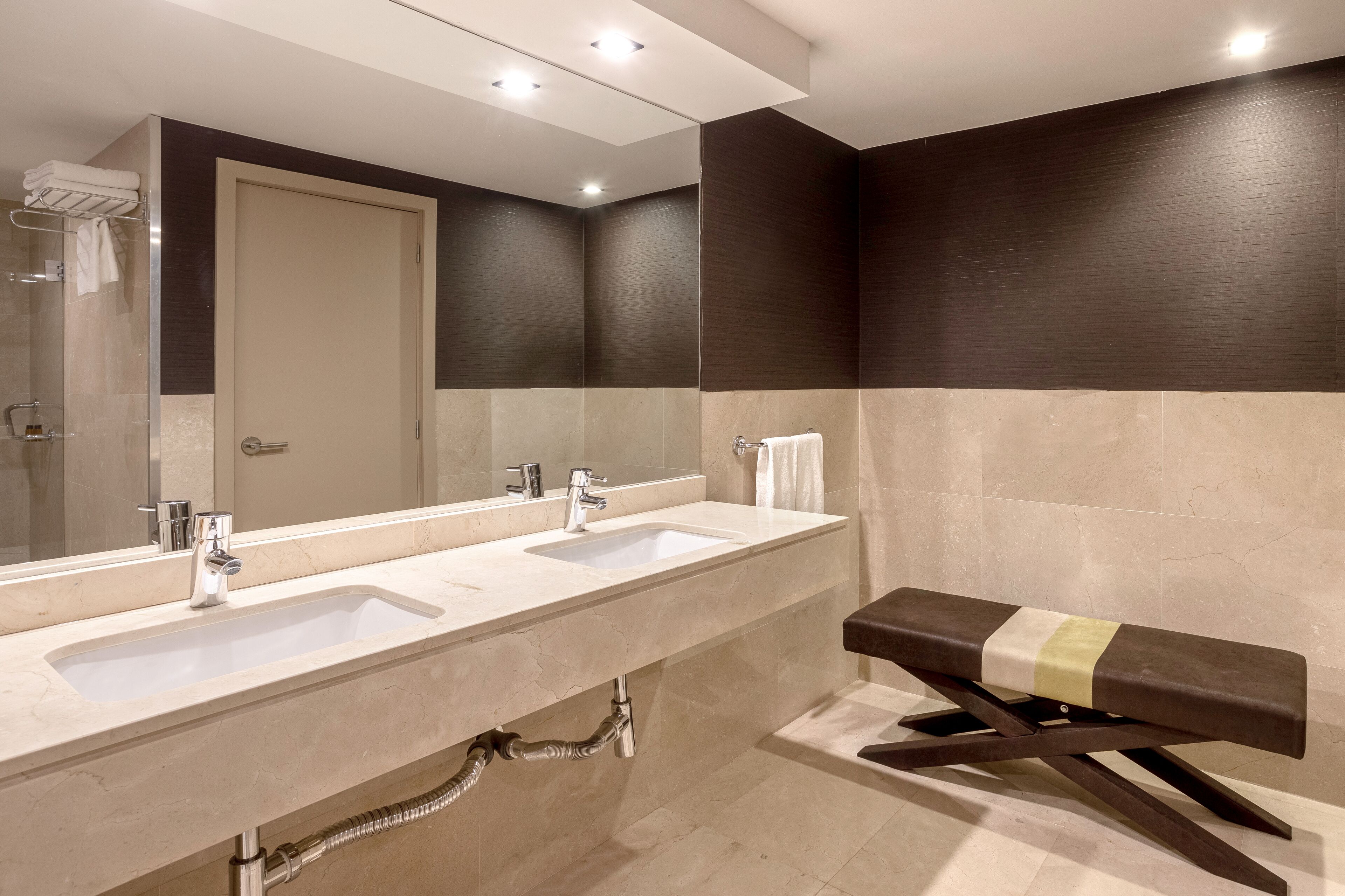 Un baño moderno con dos lavabos, un espejo grande y un banco.