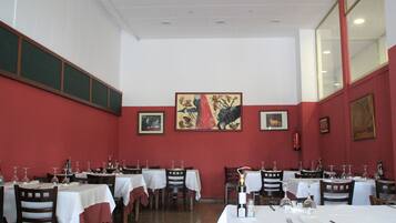 Un restaurante con mesas dispuestas para comer, paredes rojas y obras de arte enmarcadas.