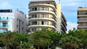 A multi-story hotel with a curved facade, located in a landscaped area with trees and rocks.