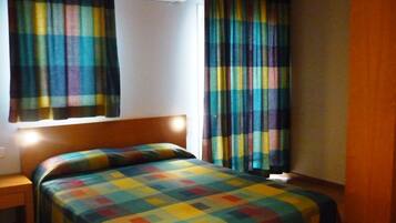 Una stanza con un letto, un comodino, una finestra con tende e un condizionatore d'aria.