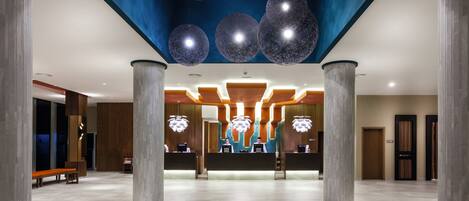 A spacious lobby with a reception desk, wooden accents, and a modern ceiling design.
