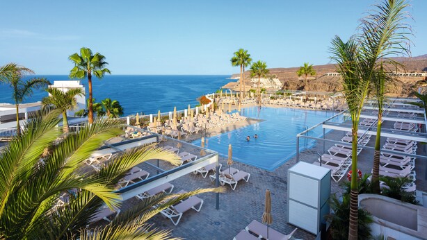 Une piscine d’hôtel avec des chaises longues, des palmiers et une vue sur l’océan.