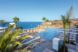 A resort pool with sun loungers, palm trees, and a view of the ocean.