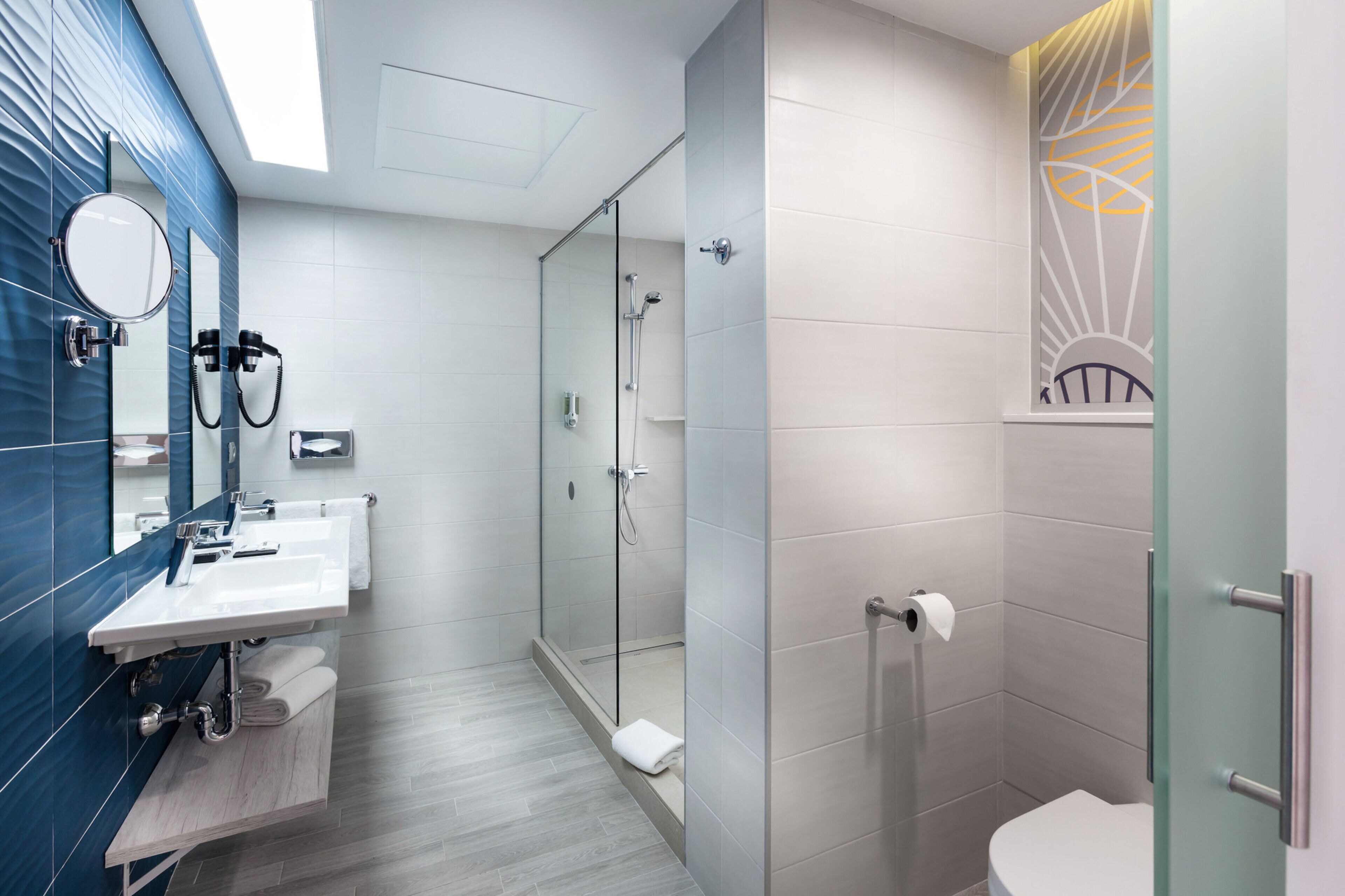 Un baño moderno con ducha envuelta en vidrio, un lavamanos con espejo y un inodoro.