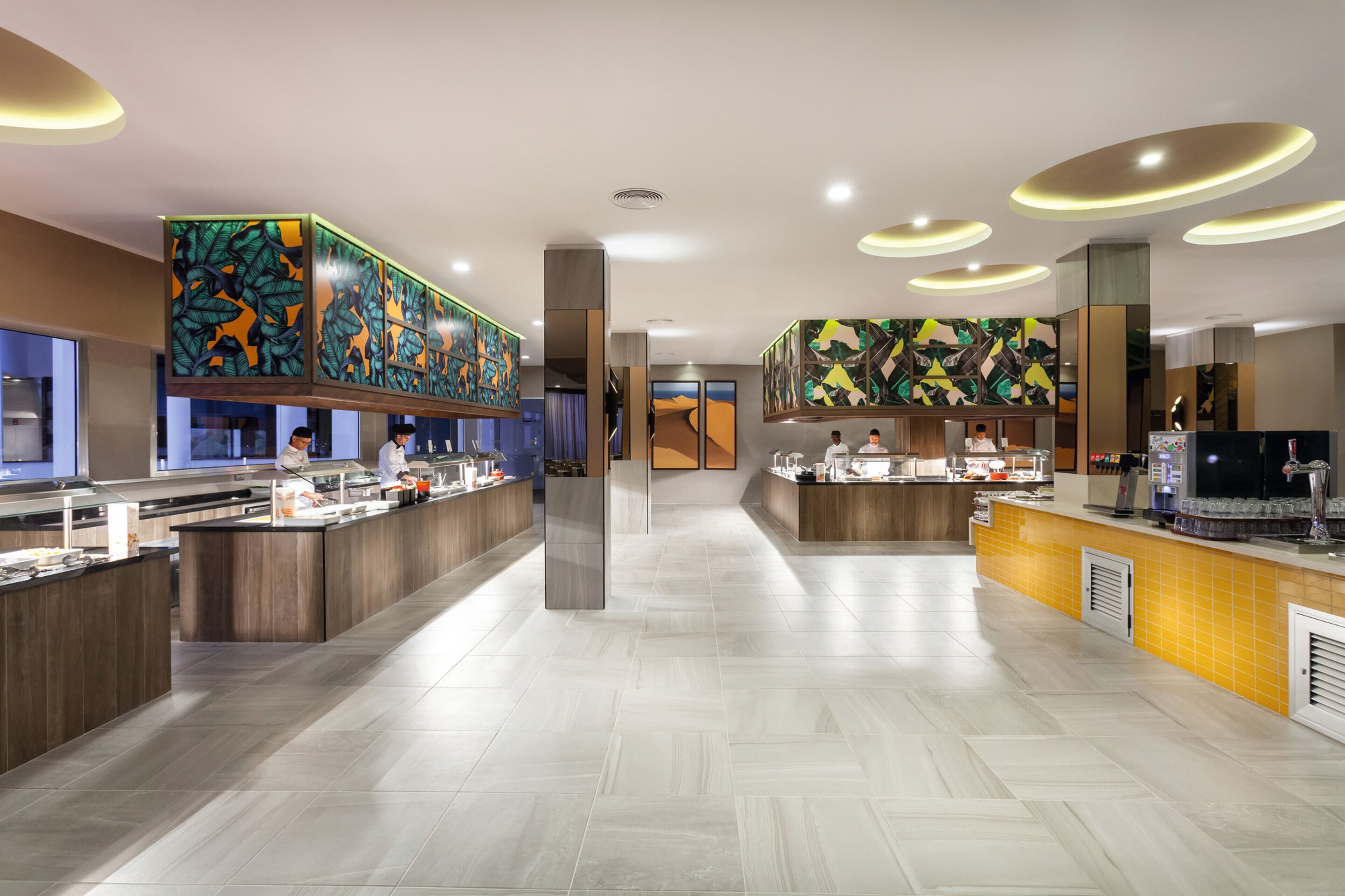 A modern hotel lobby with a long reception desk, a coffee bar, and a large mural on the wall.