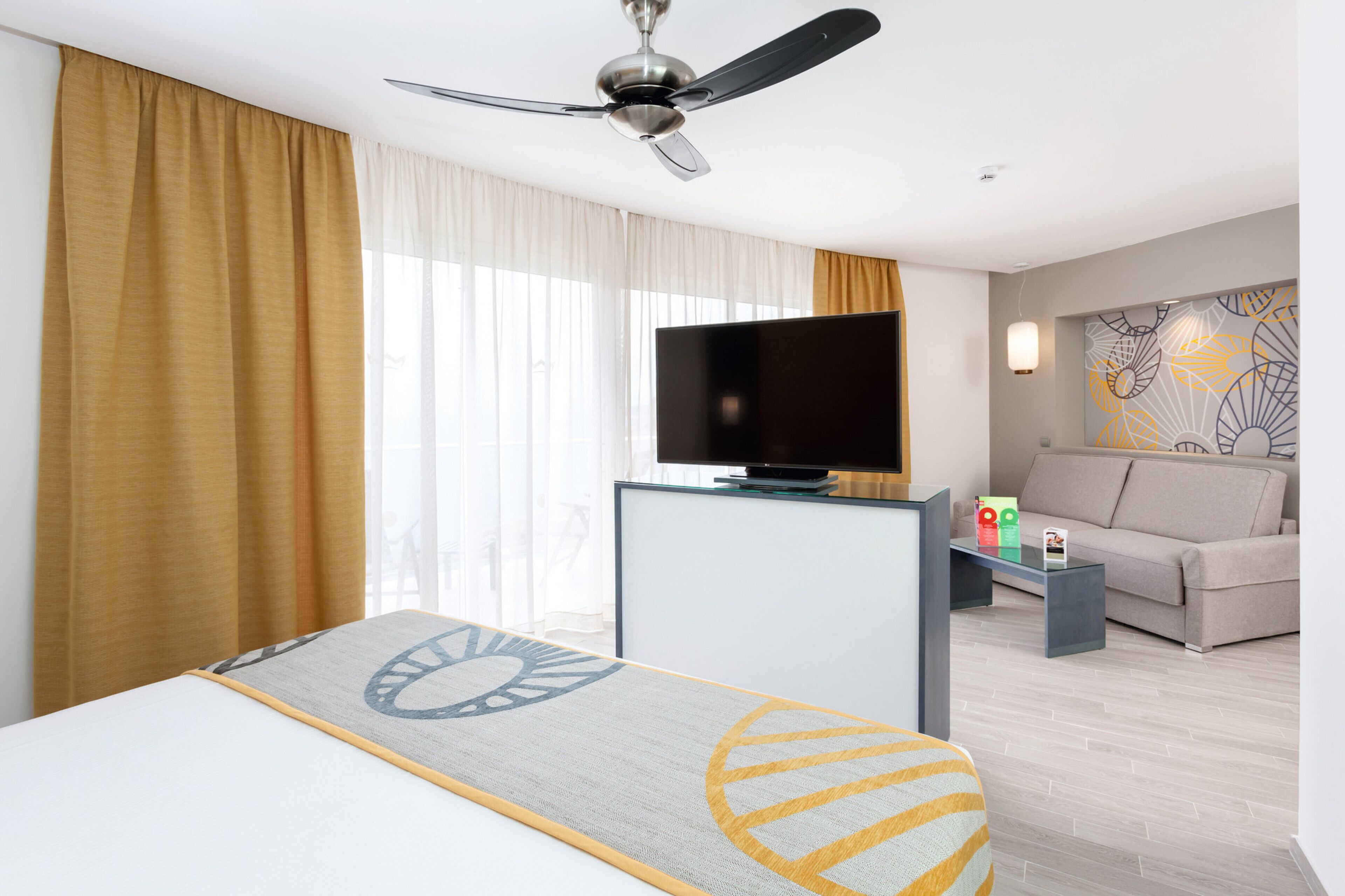 Una habitación de hotel con cama, televisión, sofá y ventilador de techo.