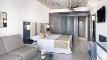 Una habitación de hotel moderna con una cama grande, un sofá, una mesa de centro de vidrio y un ventilador de techo.