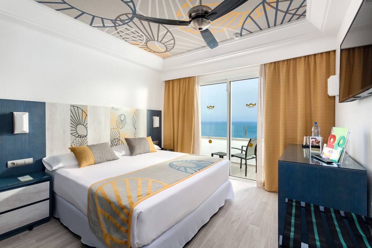 Ein Hotelzimmer mit Bett, Schreibtisch, Stuhl und Blick aufs Meer.