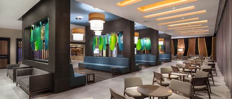 A modern hotel lobby with seating areas, tables, and a reception desk.