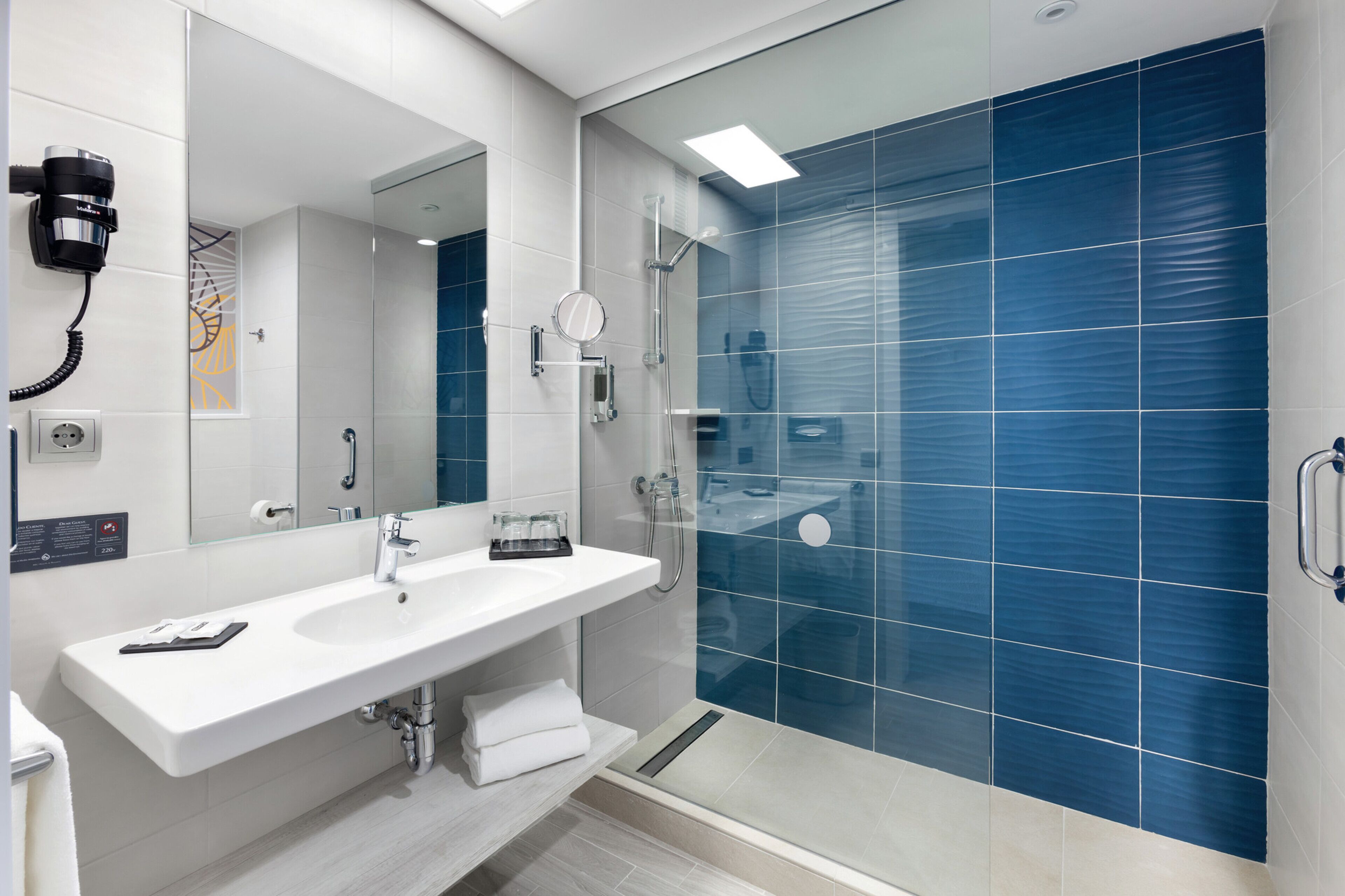 Un baño moderno con lavamanos blanco, espejo y cabina de ducha de vidrio.