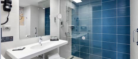 A modern bathroom with a white sink, mirror, and glass shower enclosure.