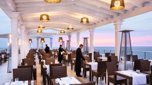 Un restaurant avec des chaises et des tables en osier, des piliers blancs et des lampes suspendues.