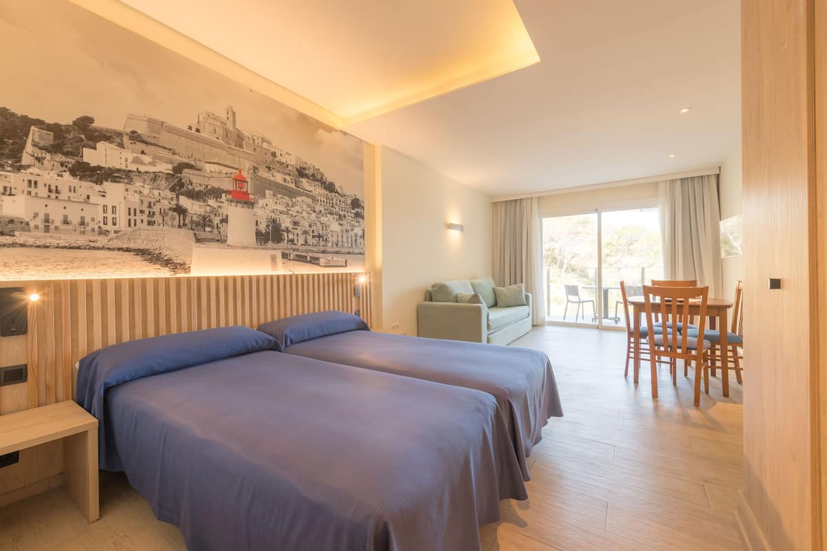 A hotel room with two beds, a dining area, and a large window.