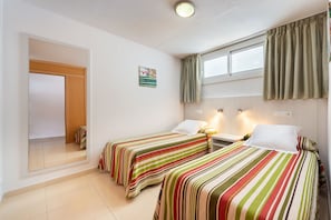 A room with two beds, a window with curtains, a painting on the wall, and a mirror. - Apartamentos Lido (Ibiza Town)