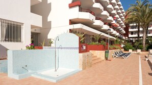 Uma área de piscina com um muro revestido, uma banheira de hidromassagem e espreguiçadeiras.